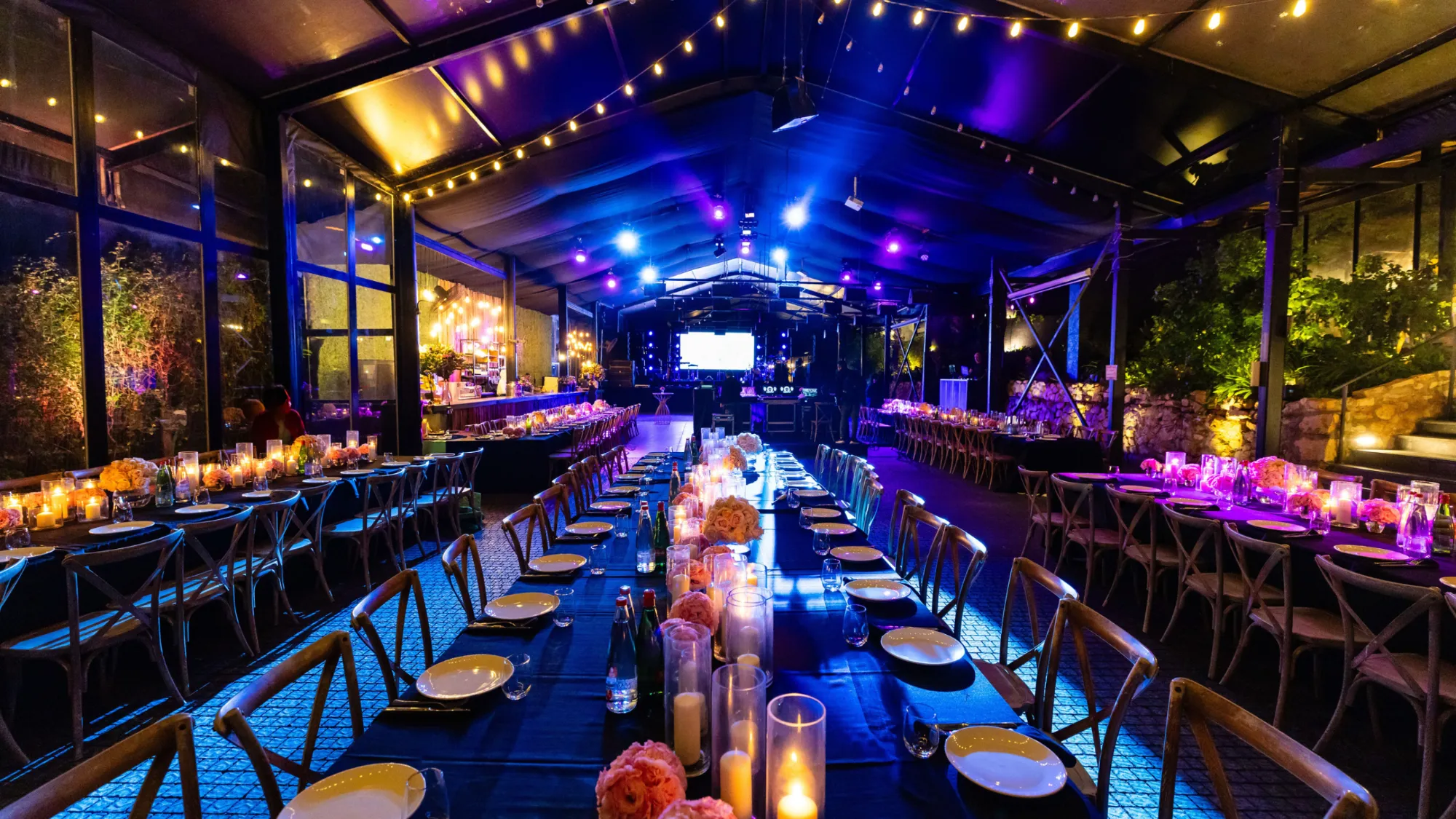 Long candlelit tables under festoon lighting at an exclusive evening event in London